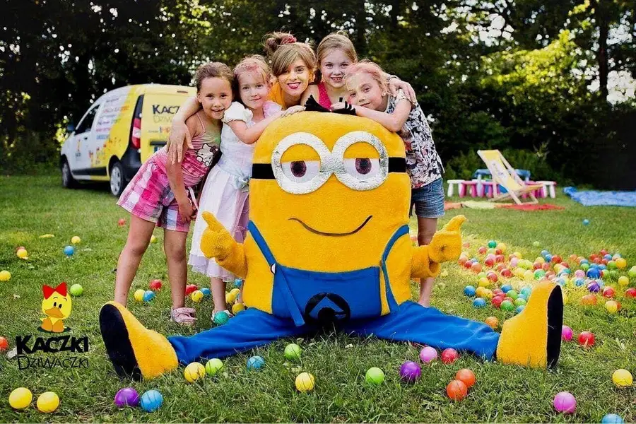 Maskotka Minionka i dzieci wśród kolorowych piłek na trawie podczas przyjęcia w ogrodzie