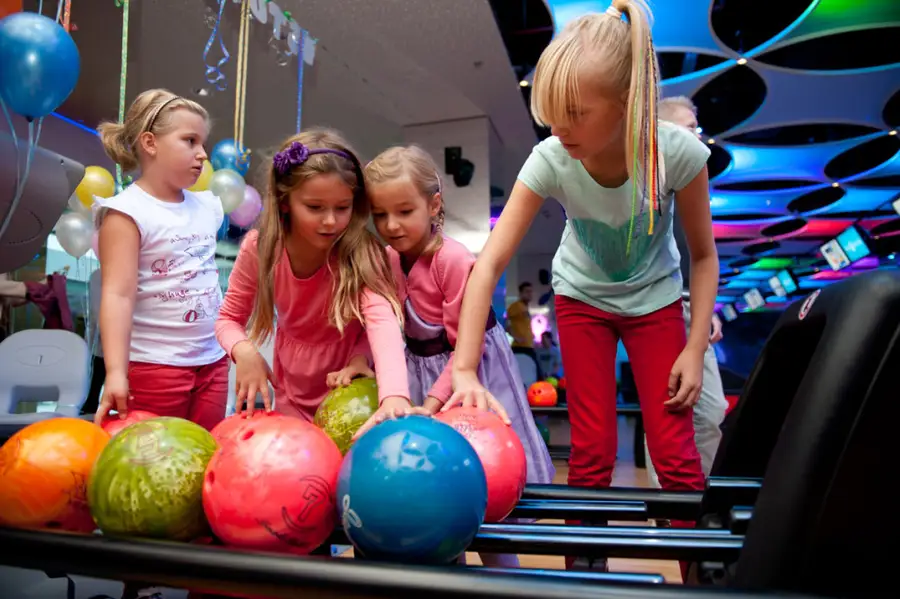 Cztery dziewczynki wybierają kolorowe kule przy torze Sky Bowling, nad nimi urodzinowe balony