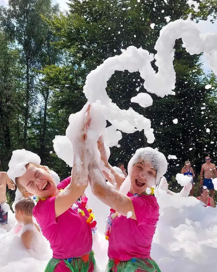 Dwie animatorki w hawajskich wiankach przybijają piątkę w chmurze piany
