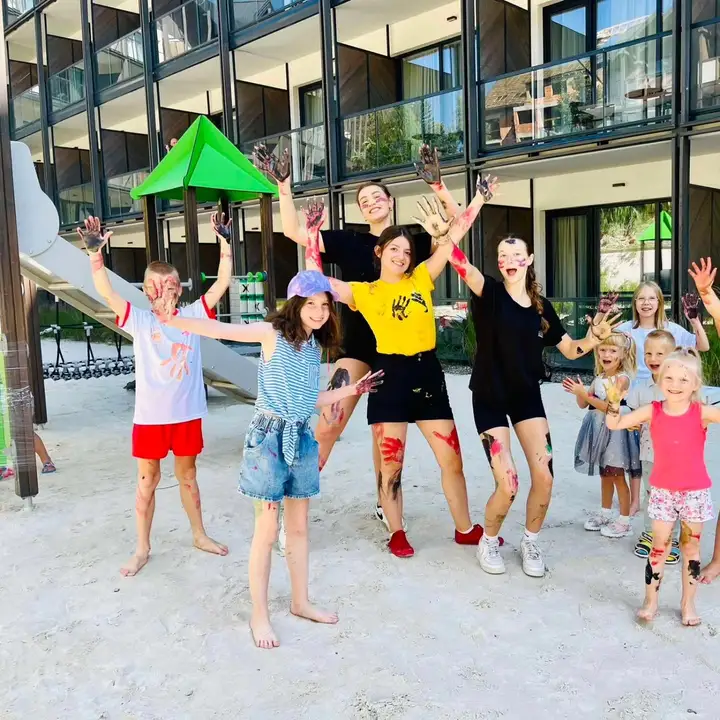 Trzy animatorki z dziećmi na hotelowym placu zabaw przed nowoczesnym budynkiem